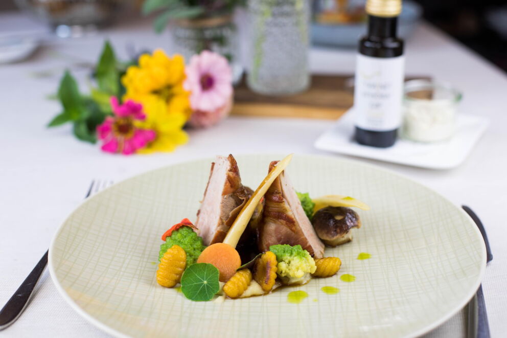 Elegant dish with vegetables, meat and edible flowers served on a stylish plate.