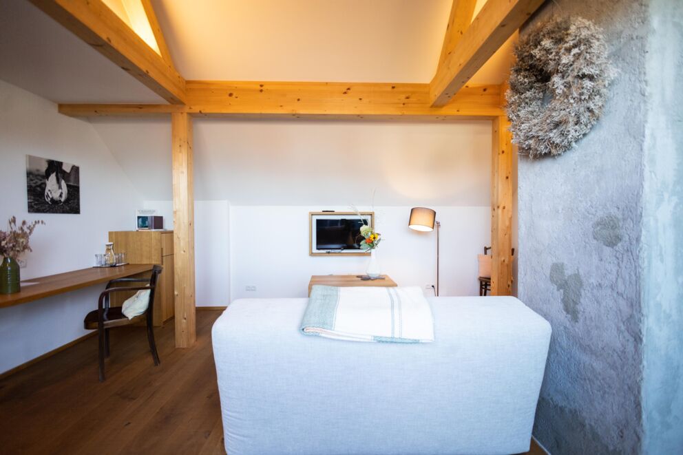 Helles Zimmer mit Holzbalken, gemütlicher Couch, TV und stilvoller Dekoration.