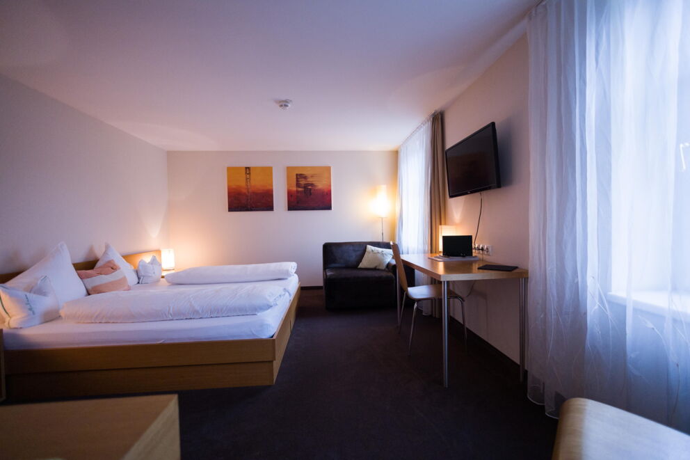 Bright double room with comfortable bed, desk and TV, discreet lighting.