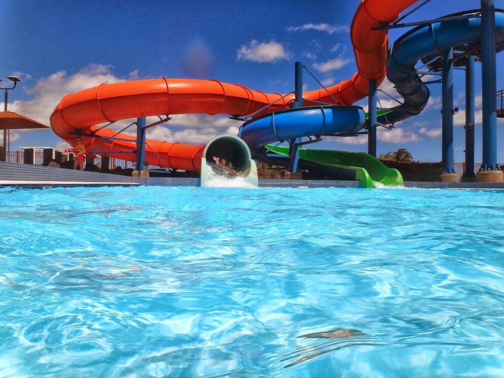 Bunte Wasserrutschen münden in ein großes Schwimmbecken unter blauem Himmel.