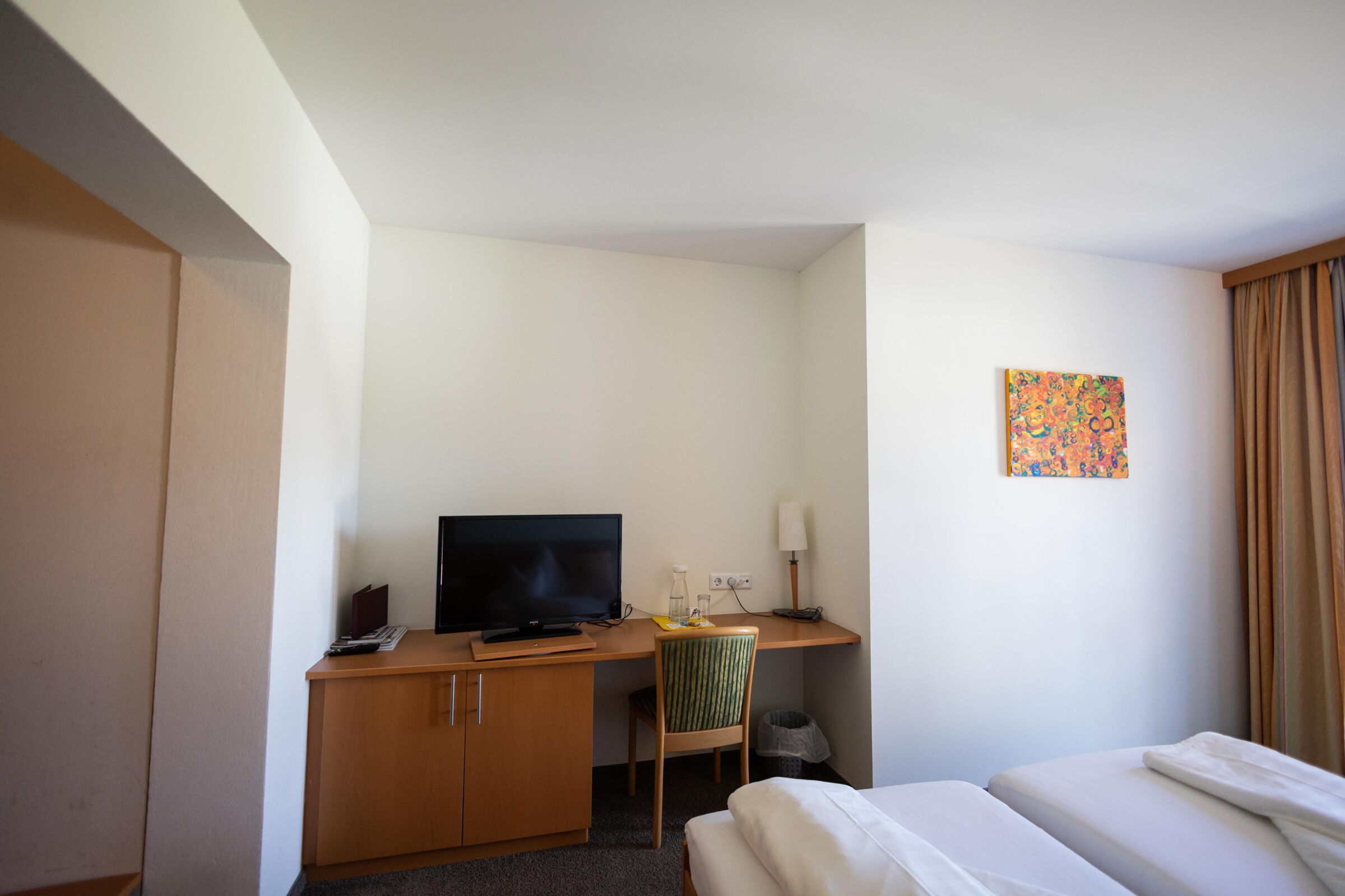Bright room with double bed, desk, TV and colorful mural.
