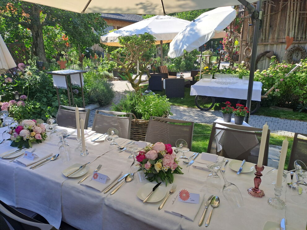 Festlich gedeckter Tisch im Garten mit Blumen und Kerzen.
