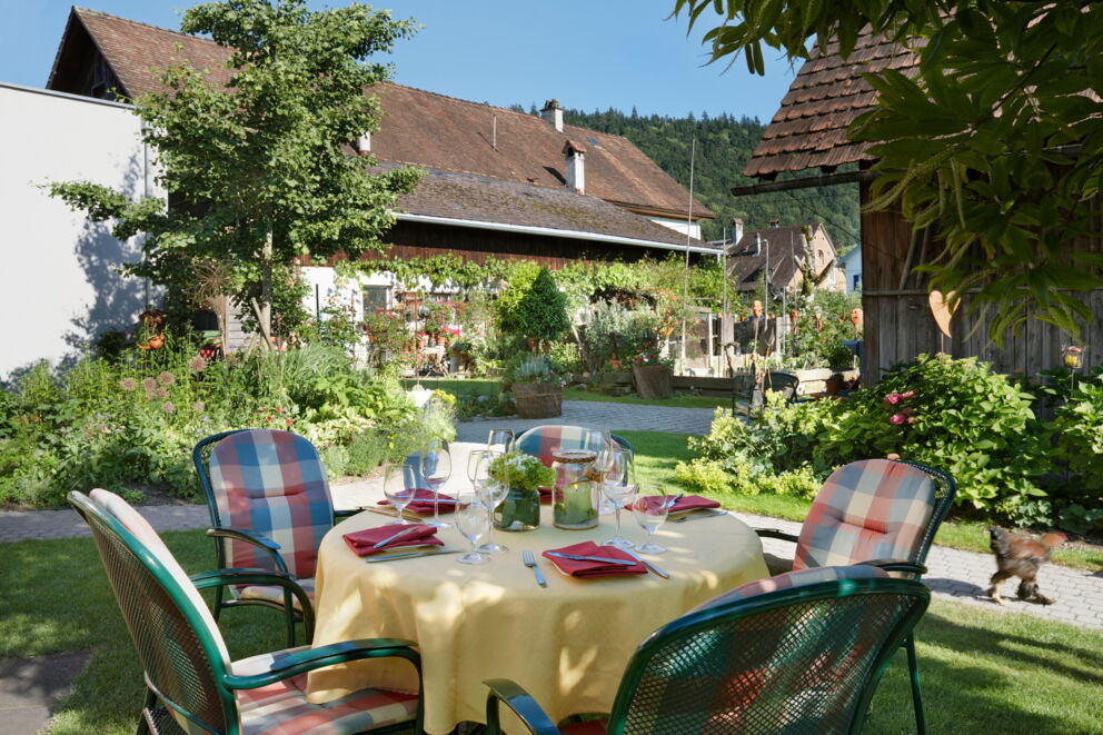 Garden table with colorful chairs and lush greenery in the background.