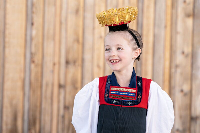 Mädchen in traditioneller Vorarlberger Tracht vor Holzwand, lächelnd porträtiert.