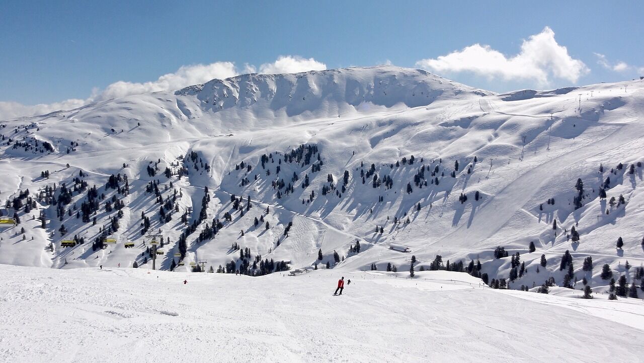 Snow-covered mountain landscape with skiers under a blue sky and sunshine.